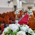 Corredor cerimonial para casamento com colunas de vidro e arranjos florais brancos disponível para locação na Zona Leste de São Paulo.